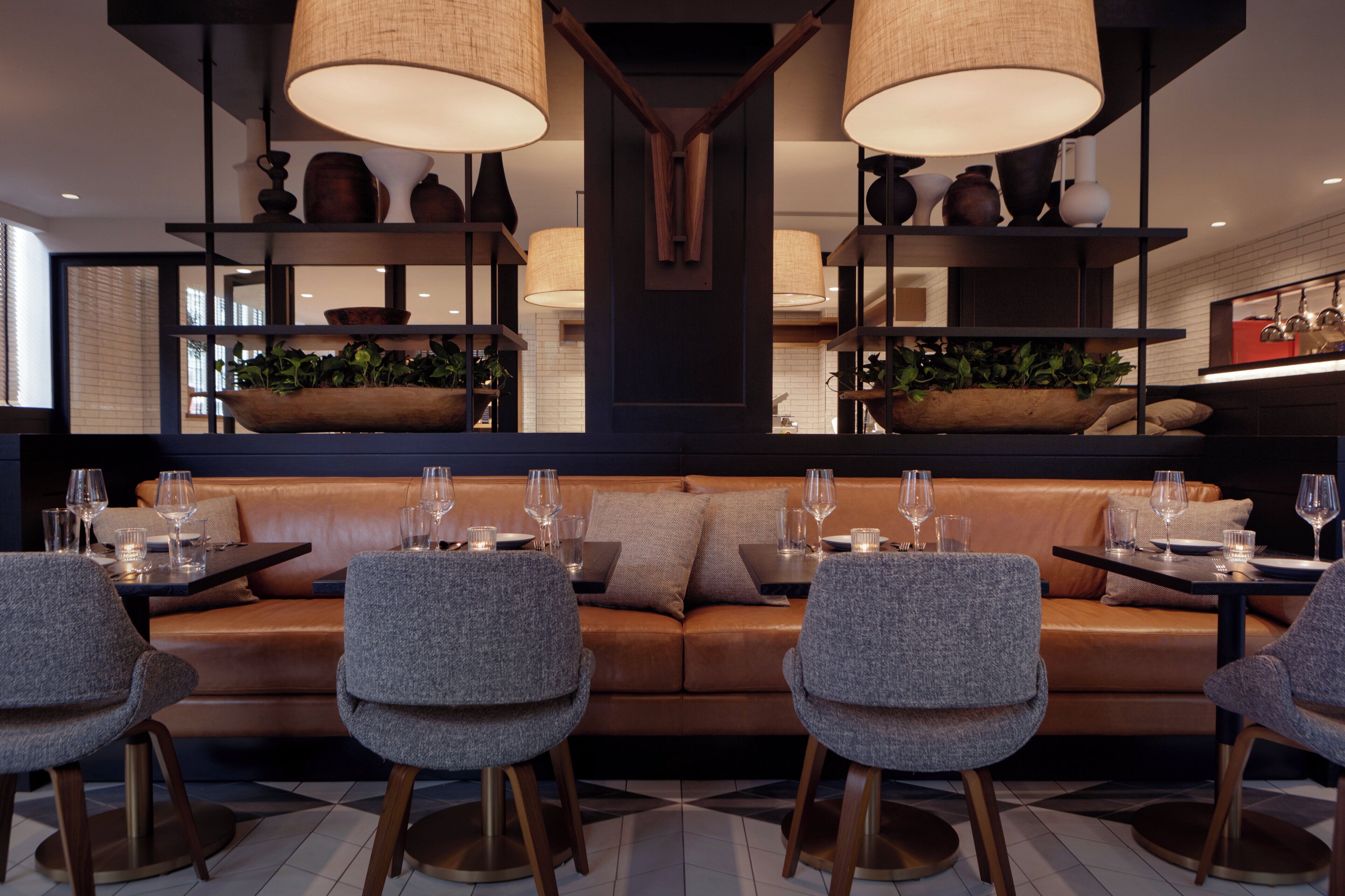 A modern dining area with a sofa and chairs, a table set with glasses and cutlery, and decorative plants.