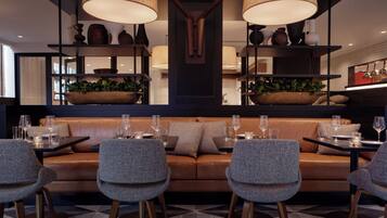 A modern dining area with a sofa and chairs, a table set with glasses and cutlery, and decorative plants.