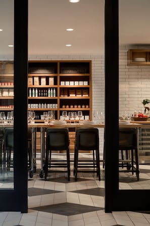 A bar area with a brick wall, shelves with bottles, glasses, and a table with chairs. - Kimpton Harper Hotel by IHG (Fort Worth)