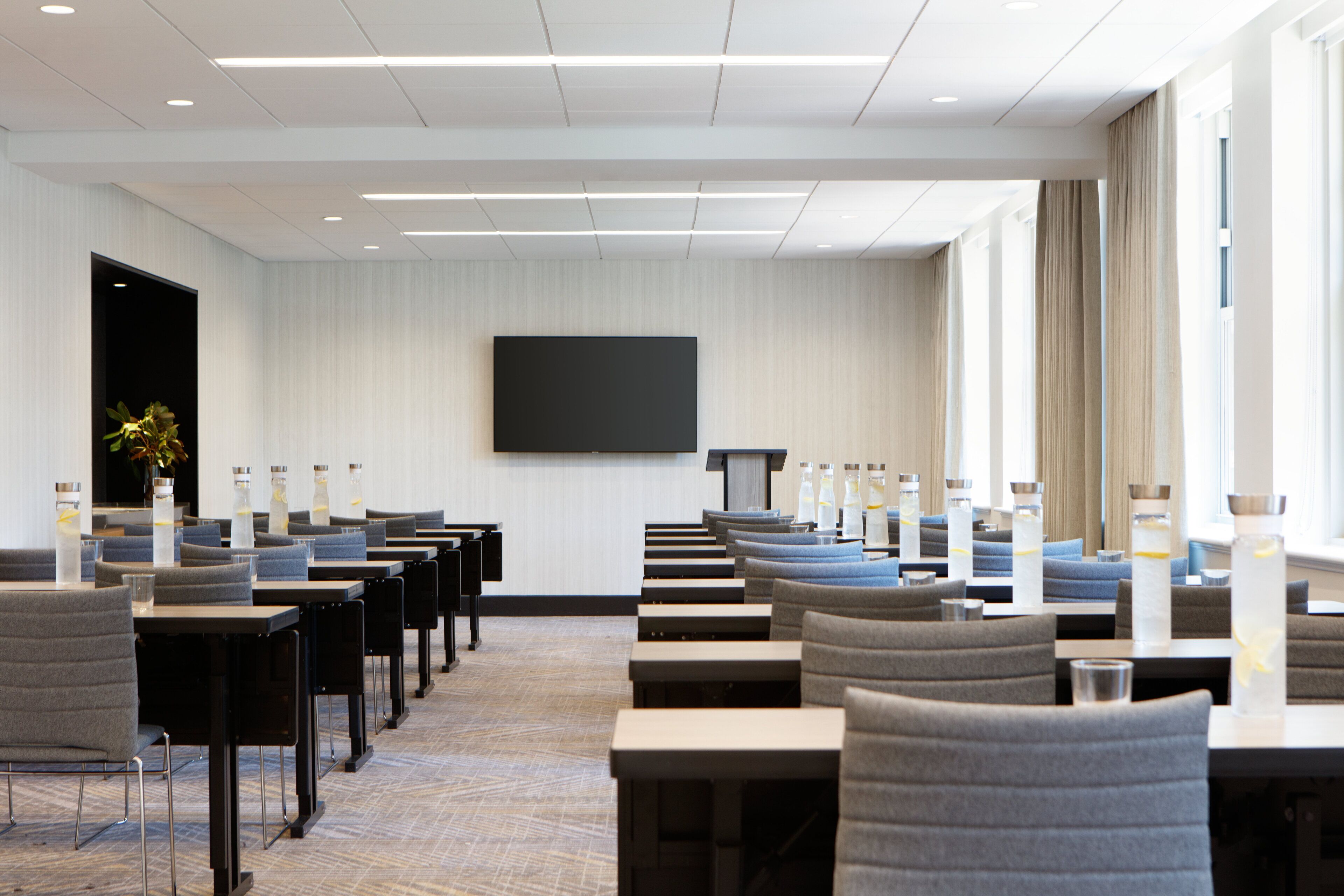 Une salle de conférence avec des rangées de tables et de chaises, un grand écran et un pupitre.