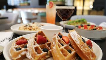 A table with waffles topped with strawberries and blueberries, a cocktail, and a bowl of salad.