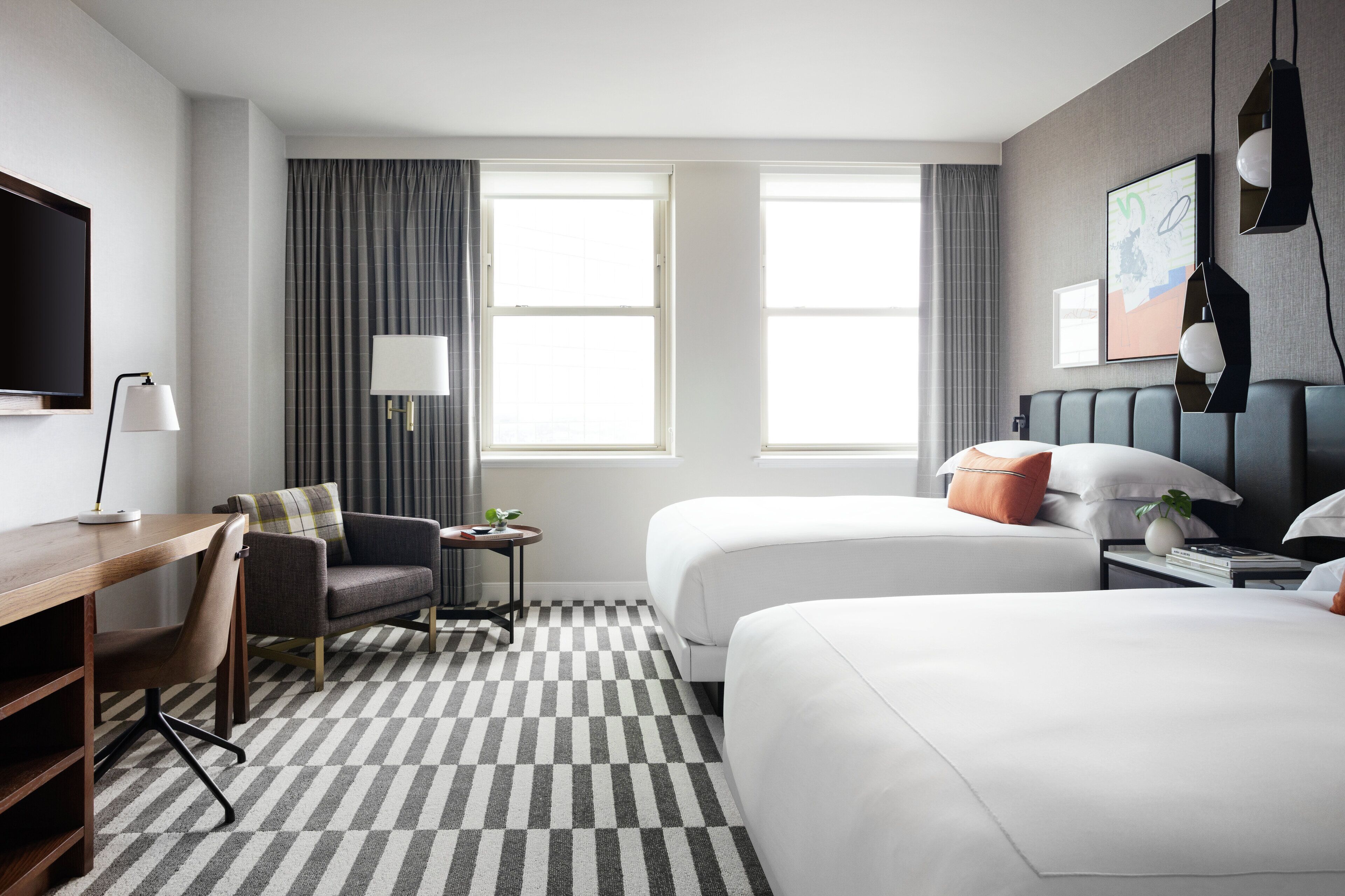 A hotel room with two beds, a desk, a chair, a TV, and a window with curtains.