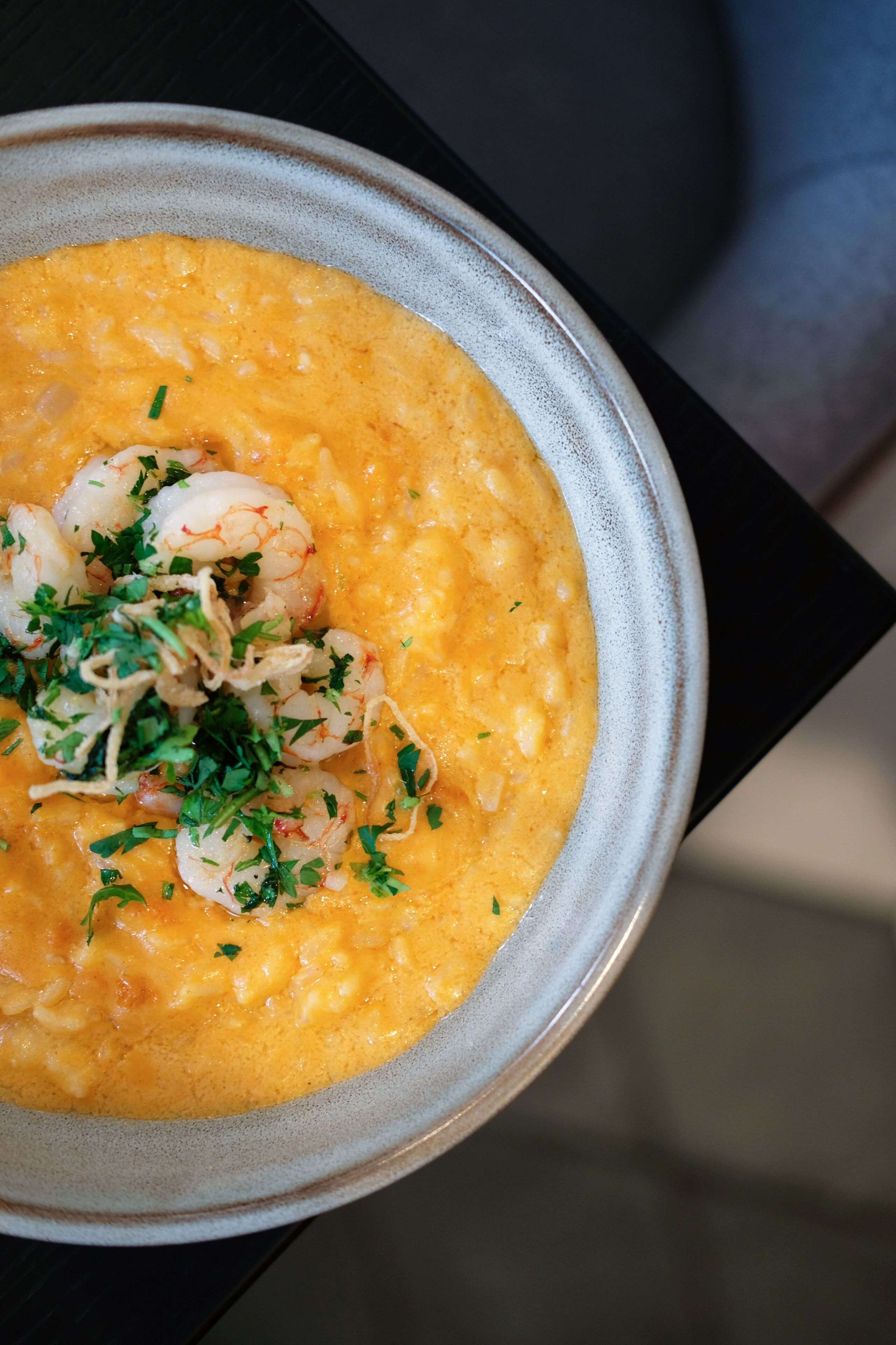 A bowl of creamy soup with shrimp and herbs.