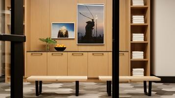 A modern kitchen with wooden cabinets, a countertop, and two benches. There are two framed pictures on the wall, a potted plant, and a bowl of fruit on the counter.