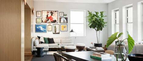 A modern living room with a sofa, coffee table, and a dining area with chairs and a table.