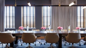 A conference room with a long table, six chairs, and vases with pink flowers.