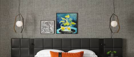 Quarto moderno com cabeceira preta, roupa de cama branca e uma única almofada laranja. Há duas luminárias fixadas na parede e uma obra de arte emoldurada acima da cama.