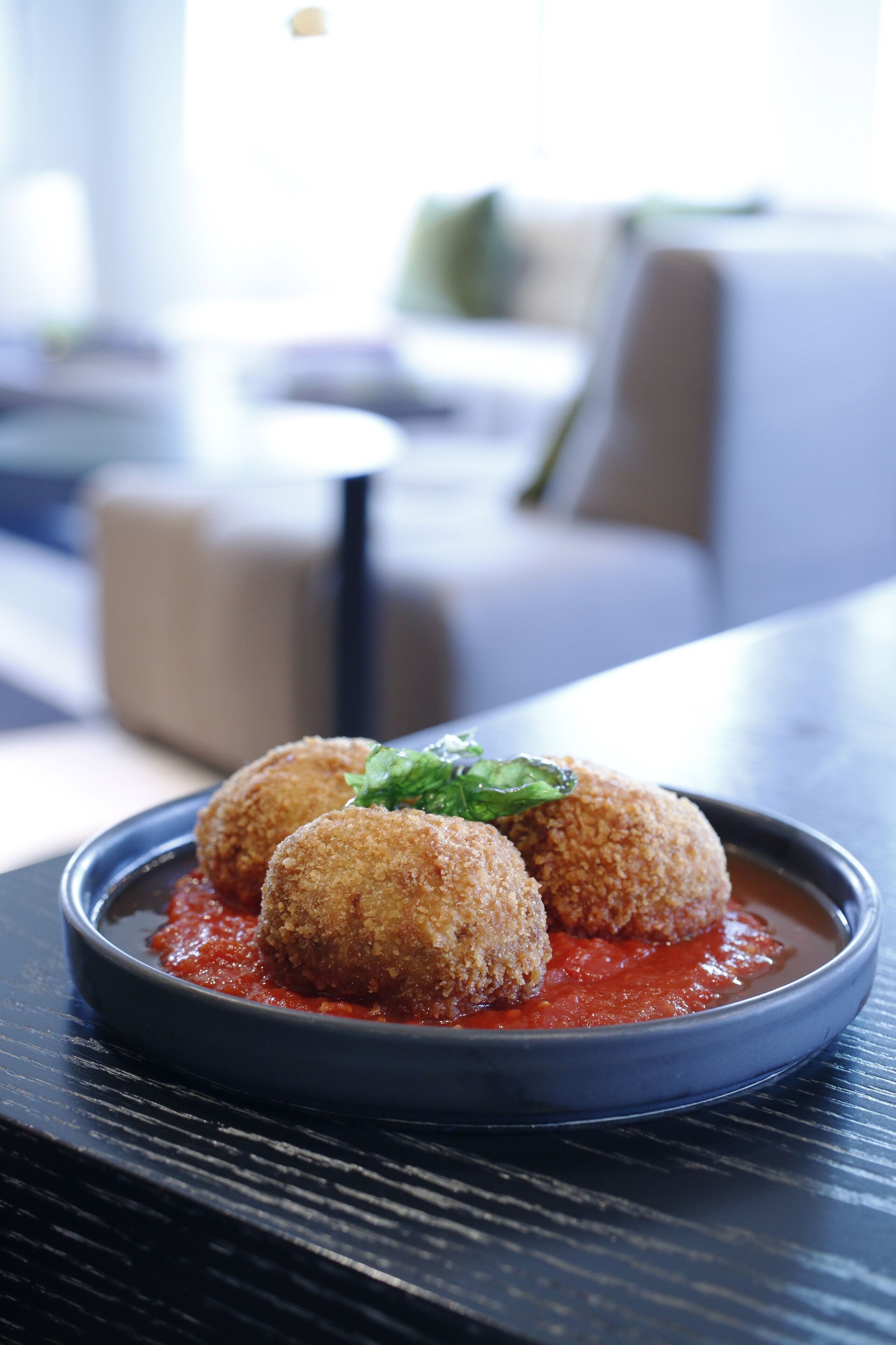 A plate of croquettes with a red sauce and a garnish, placed on a dark table in a modern dining area.
