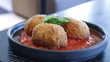 A plate of croquettes with a red sauce and a garnish, placed on a dark table in a modern dining area.