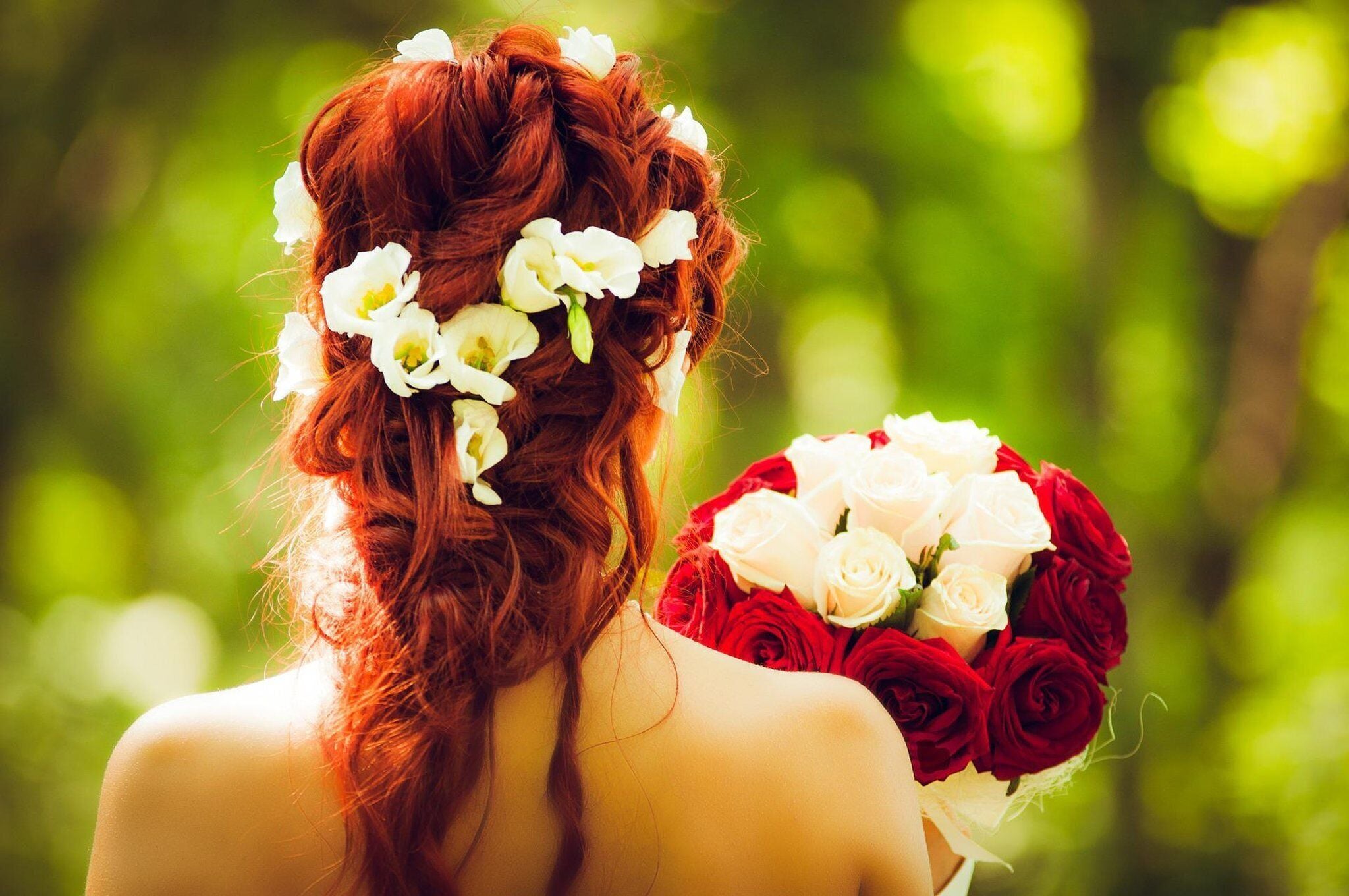Una persona de cabello pelirrojo recogido en un moño, sosteniendo un ramo de rosas rojas y blancas.