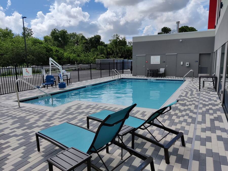 A swimming pool with a pool lift, lounge chairs, and a tiled deck.