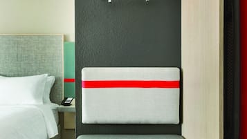 Habitación de hotel pequeña y funcional con cama, mesita de noche, escritorio con silla y armario.
