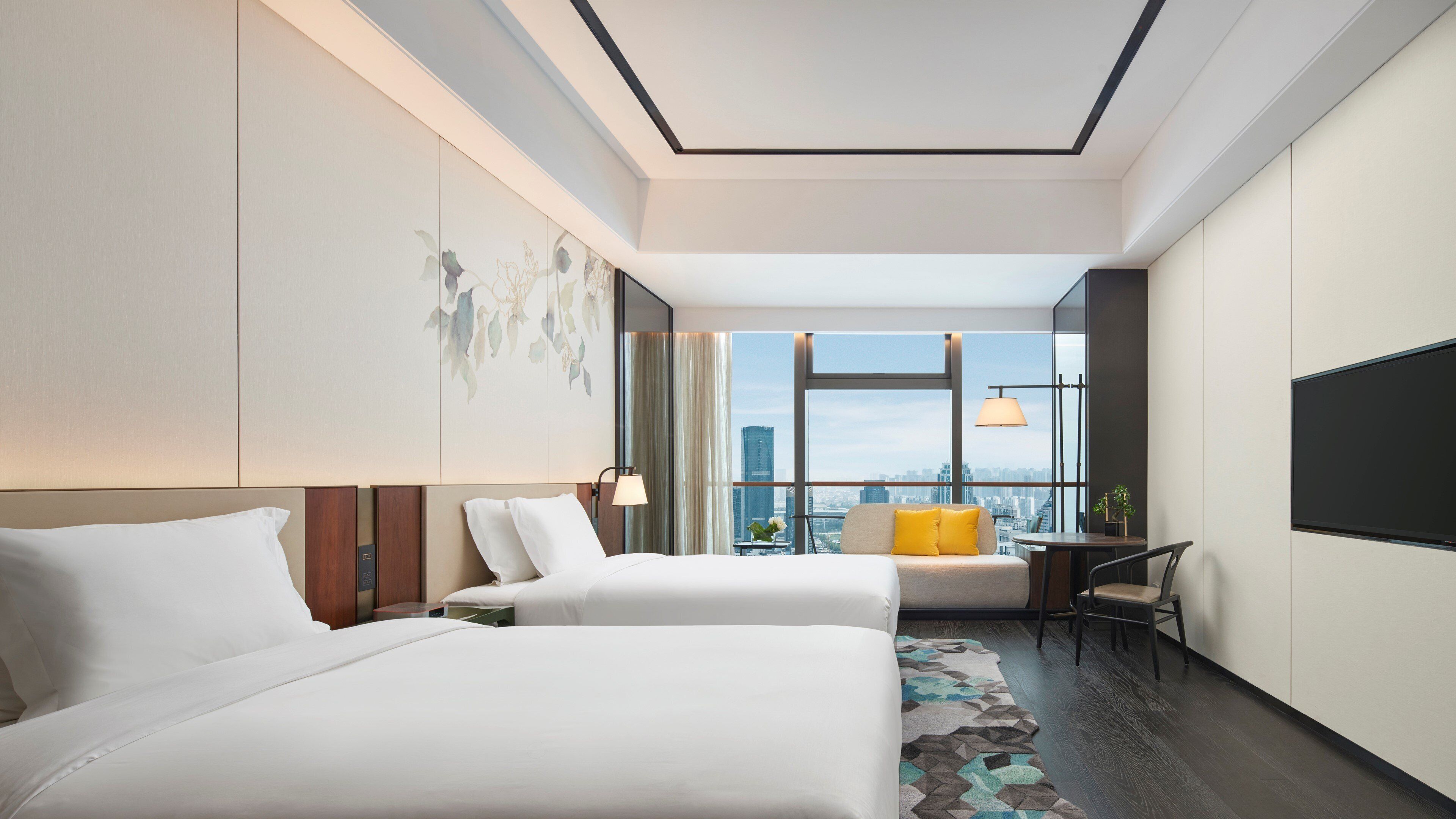 A hotel room with two beds, a city view, a desk with a chair, and a large flat-screen TV.