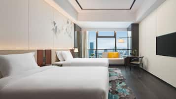 Habitación de hotel con dos camas, un escritorio, una silla, un ventanal amplio con vistas a la ciudad y una alfombra estampada.