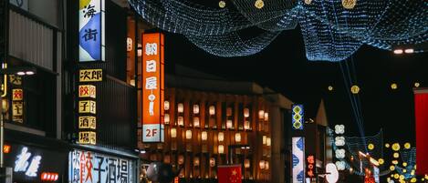 A street with illuminated signs and traditional lanterns, indicating a commercial area with shops and restaurants.