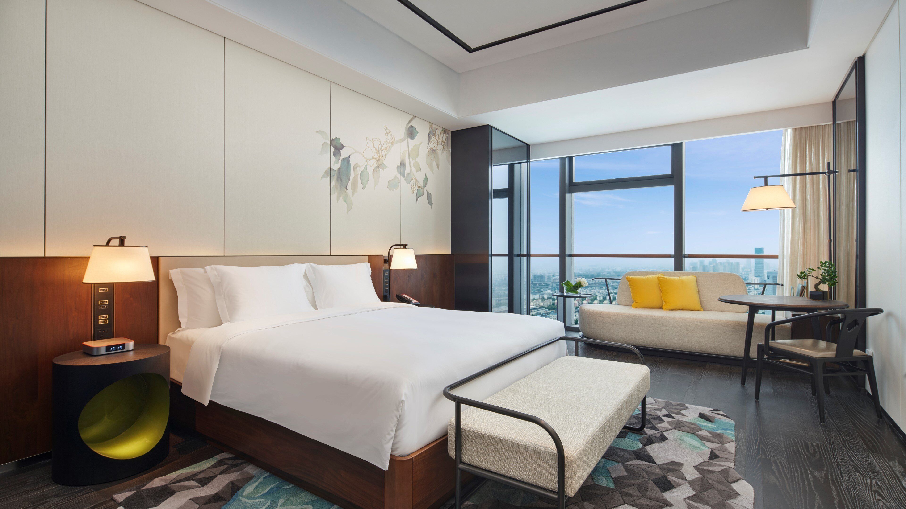 A hotel room with a large bed, a sofa, a small table, and a view of the city.