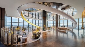 Een ruime lobby met een gebogen plafond, grote ramen met uitzicht op de stad en een receptiegedeelte met zitplaatsen.