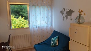 A room with a window, a bed with a blue cover, a world map wall decal, a small vase with flowers, and a radiator. - Studio - quiet seaside location with private parking (La Ciotat)
