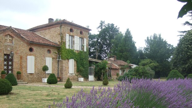 A stone building with a garden in front, including lavender bushes. - Château Pour 24 Personne (Brocas)