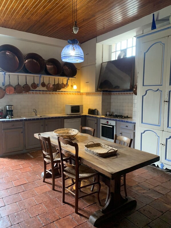 A kitchen with hanging pots, a wooden table, chairs, and a tiled floor. - Château Pour 24 Personne (Brocas)
