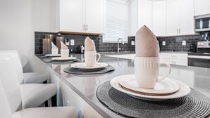 A modern kitchen with white cabinets, a black backsplash, and a dining area with white chairs and a table set with white cups and plates. - Spacious 8BD/6BA Pool Home 20048 (Kissimmee)