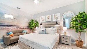 A bedroom with a bed, a sofa, a nightstand, a lamp, and two potted plants. - Spacious 8BD/6BA Pool Home 20048 (Kissimmee)