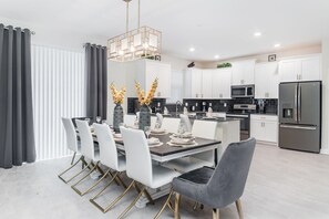 Une cuisine moderne avec des meubles blancs, un réfrigérateur en acier inoxydable et un coin repas comprenant une table foncée et des chaises blanches.
