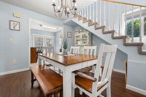 A dining area with a wooden table and white chairs, a staircase with white railings, and a chandelier.