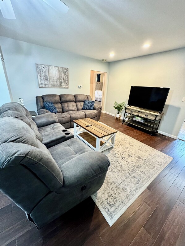 A living room with a sectional sofa, a coffee table, a flat-screen TV, and a patterned rug.