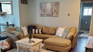 Un salon avec un canapé d’angle beige, une table basse blanche et un tapis à motifs.