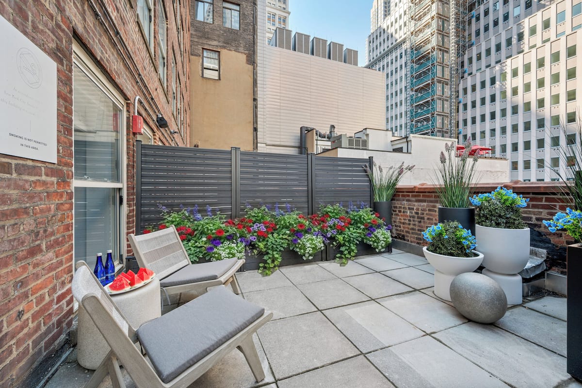 A rooftop patio with outdoor seating, potted plants, and a brick building in the background.