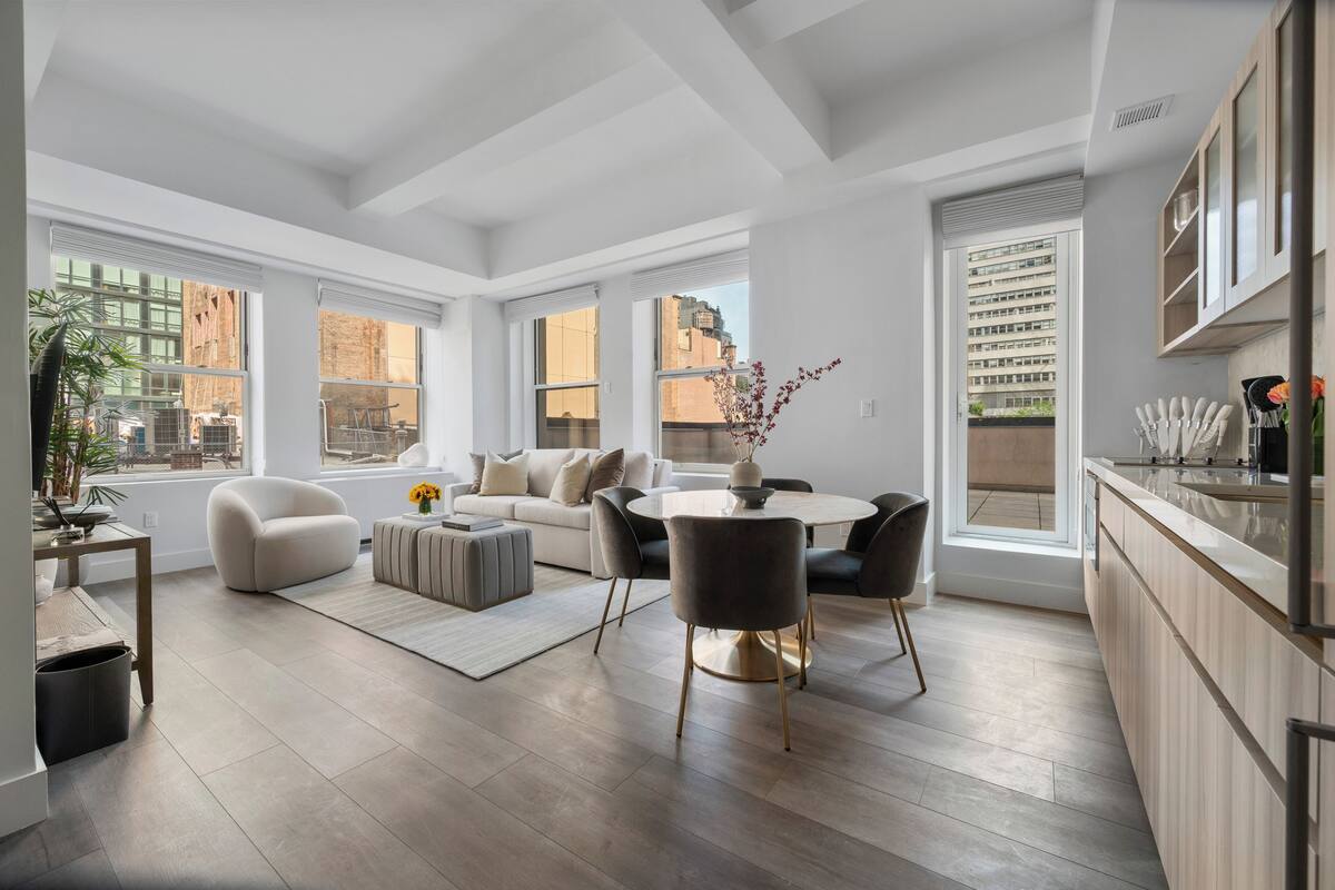 A spacious living area with a sofa, coffee table, and dining table, large windows, and a kitchen with modern appliances.