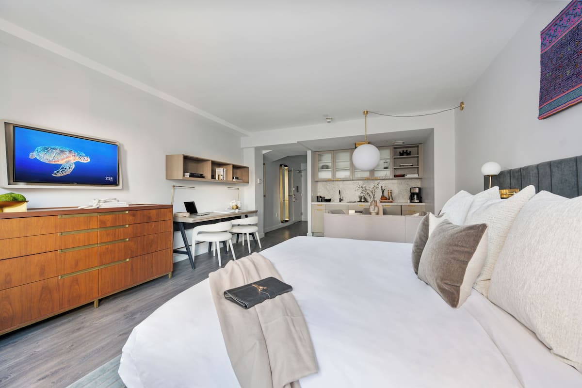 A modern hotel room with a large bed, a desk with a computer, a wardrobe, and a television displaying a turtle.