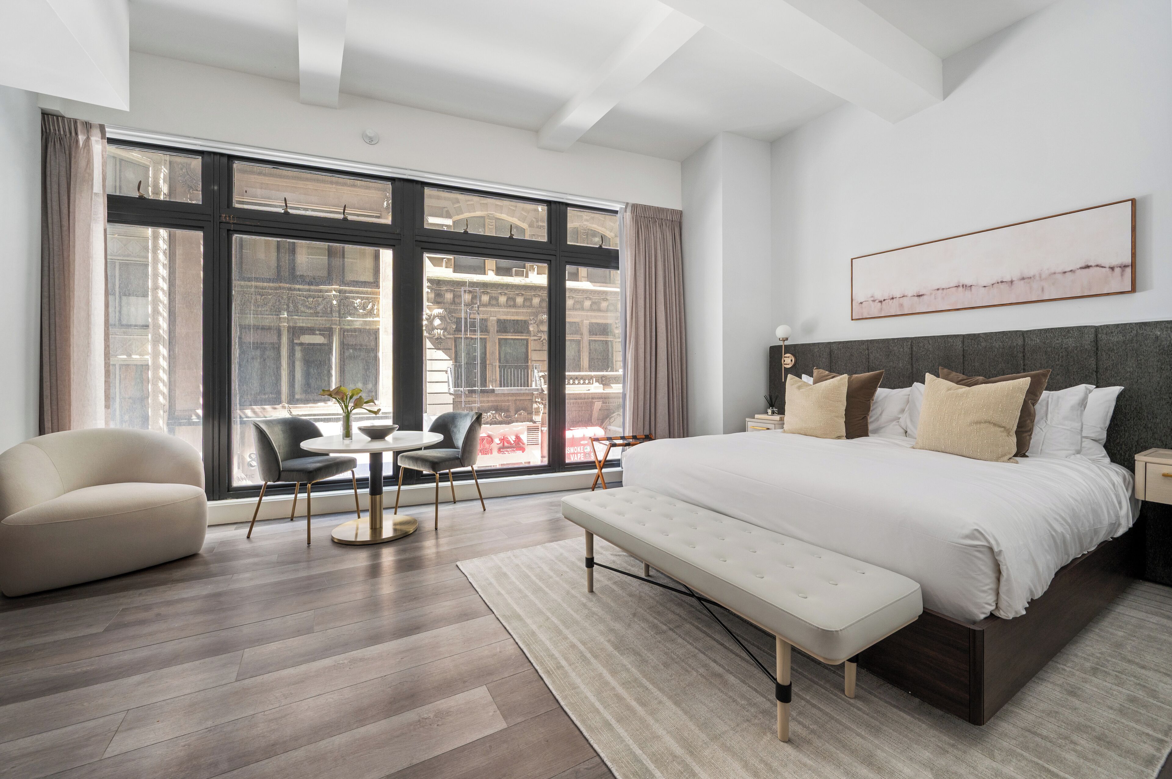 A modern bedroom with a large bed, a sofa, a dining table, and a view of the city.