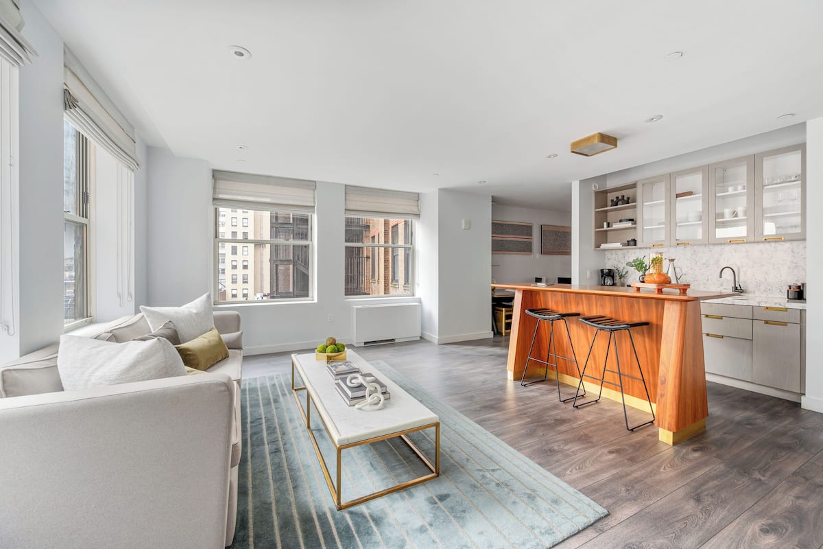 A modern apartment with a kitchen, dining area, and living room. It features large windows, a wooden floor, and a minimalist design.