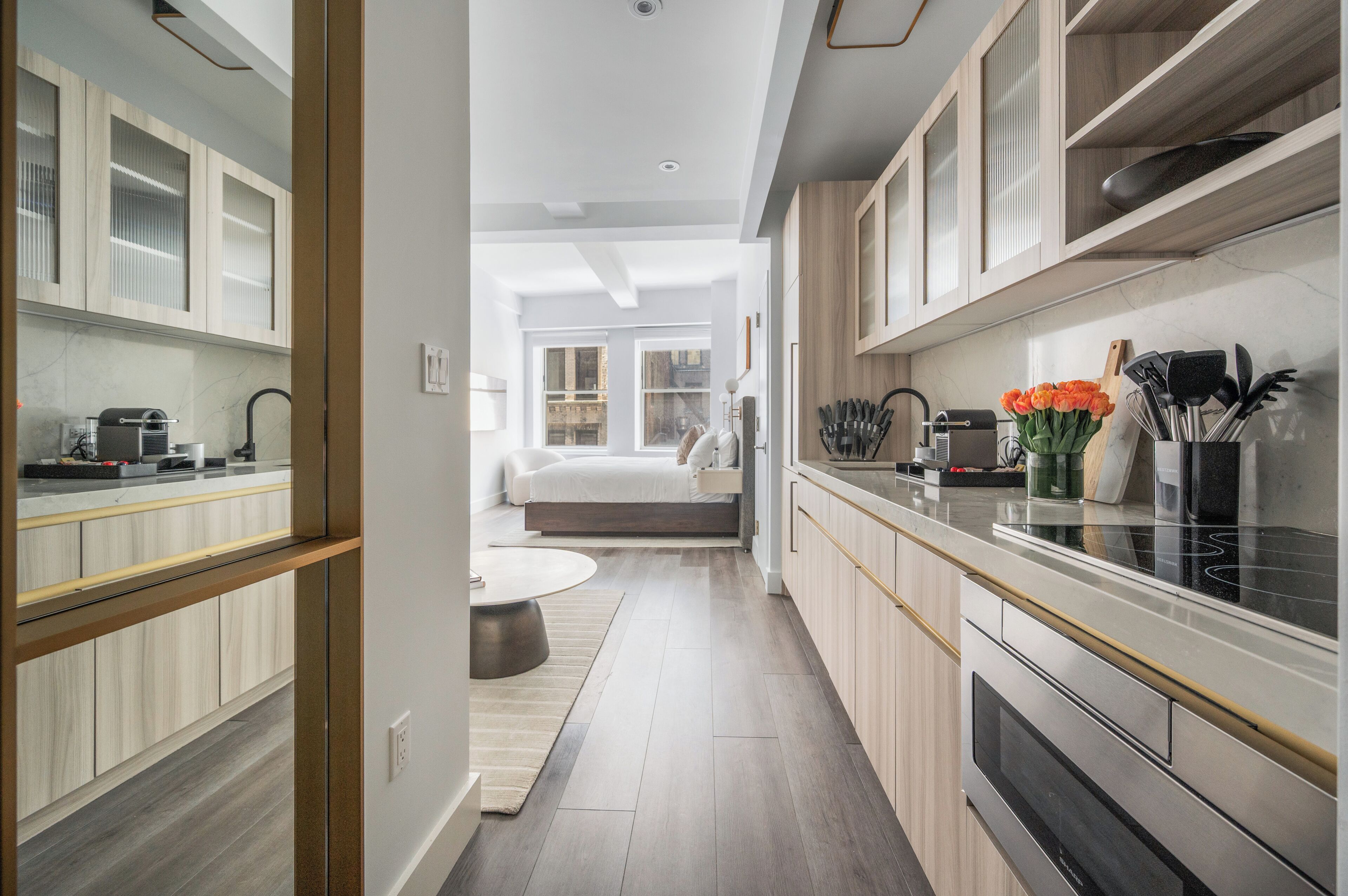 A modern kitchen with a central island, a dining area with a round table, and a bedroom with a large window.