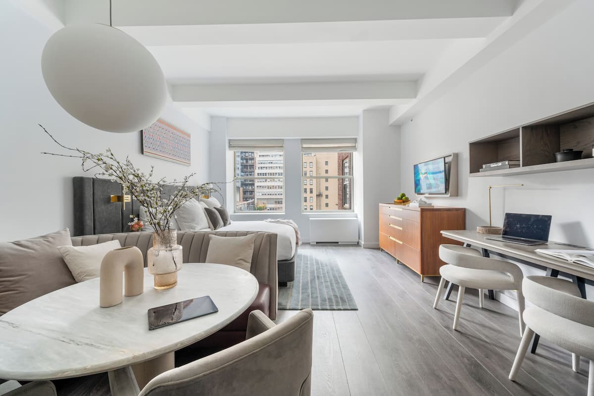 A modern apartment with a dining area, a sofa, a TV, and a desk with a laptop.