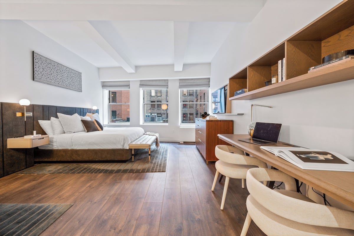 A modern bedroom with a bed, bedside tables, a desk with a laptop, and a bookshelf.