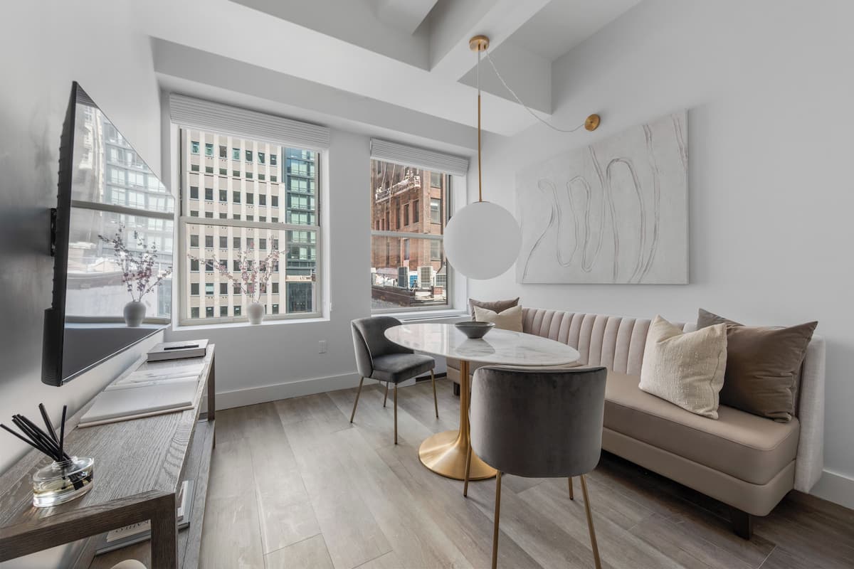 A modern living room with a sofa, a round table, a TV, and large windows with city views.