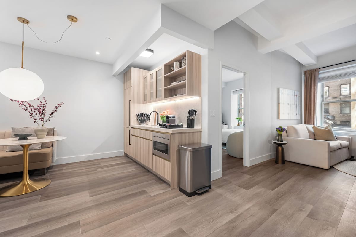 A modern kitchen with wooden cabinets, a stainless steel trash bin, and a dining area with a round table and gold base.