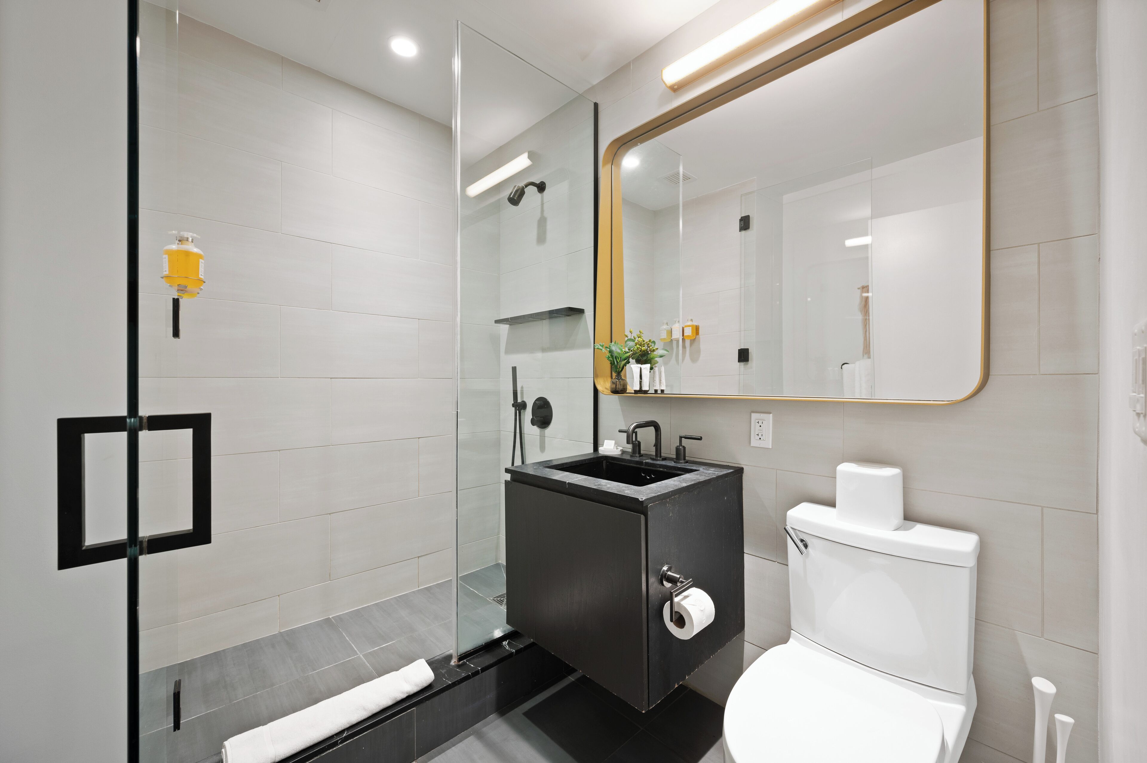 A modern bathroom with a glass shower enclosure, a black sink, and a white toilet.