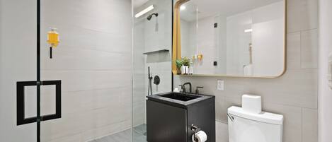 A modern bathroom with a glass shower enclosure, a black sink, and a white toilet.