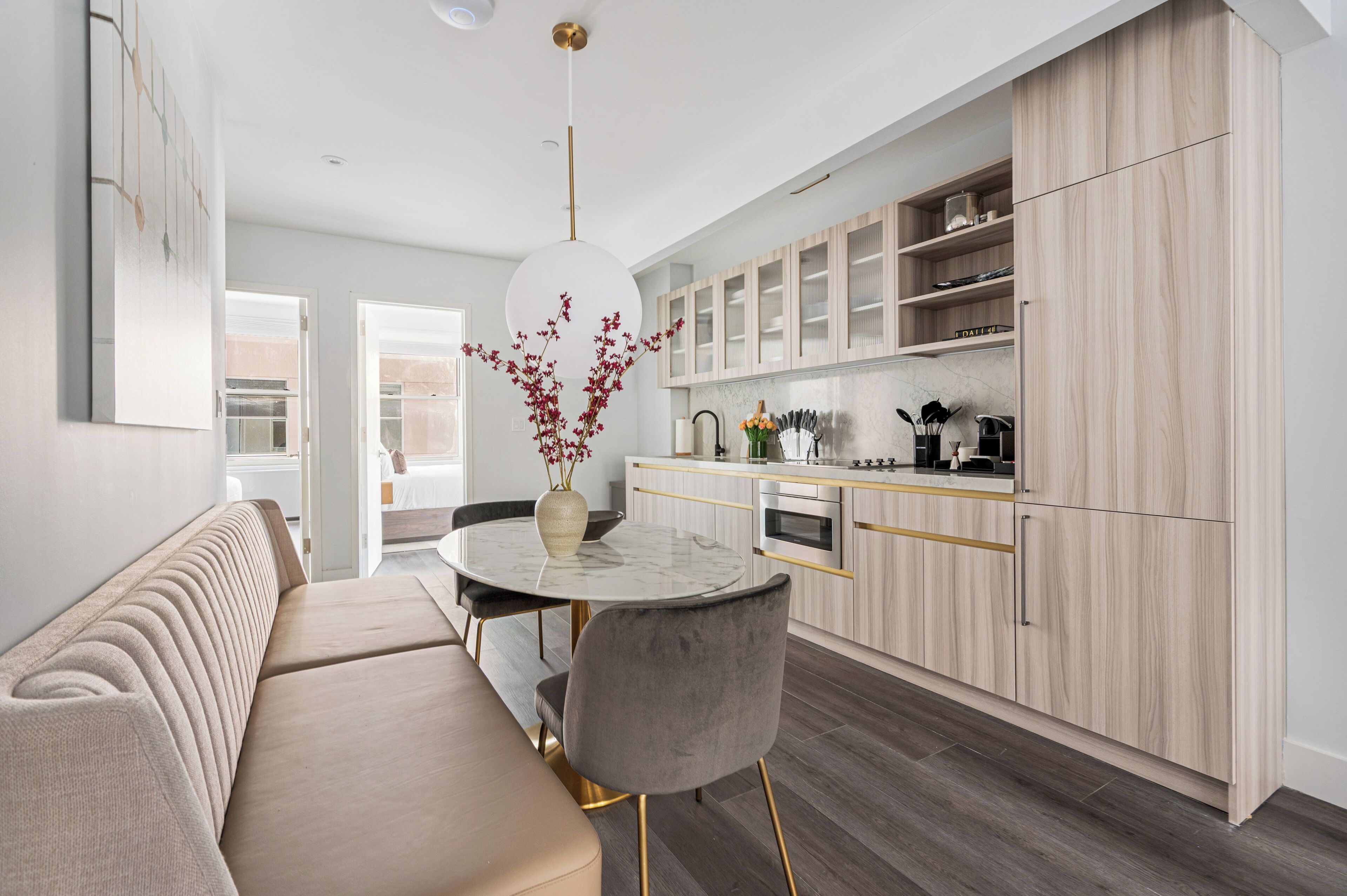 A modern kitchen with light wood cabinets, a marble countertop, and a dining area with a round table and chairs.