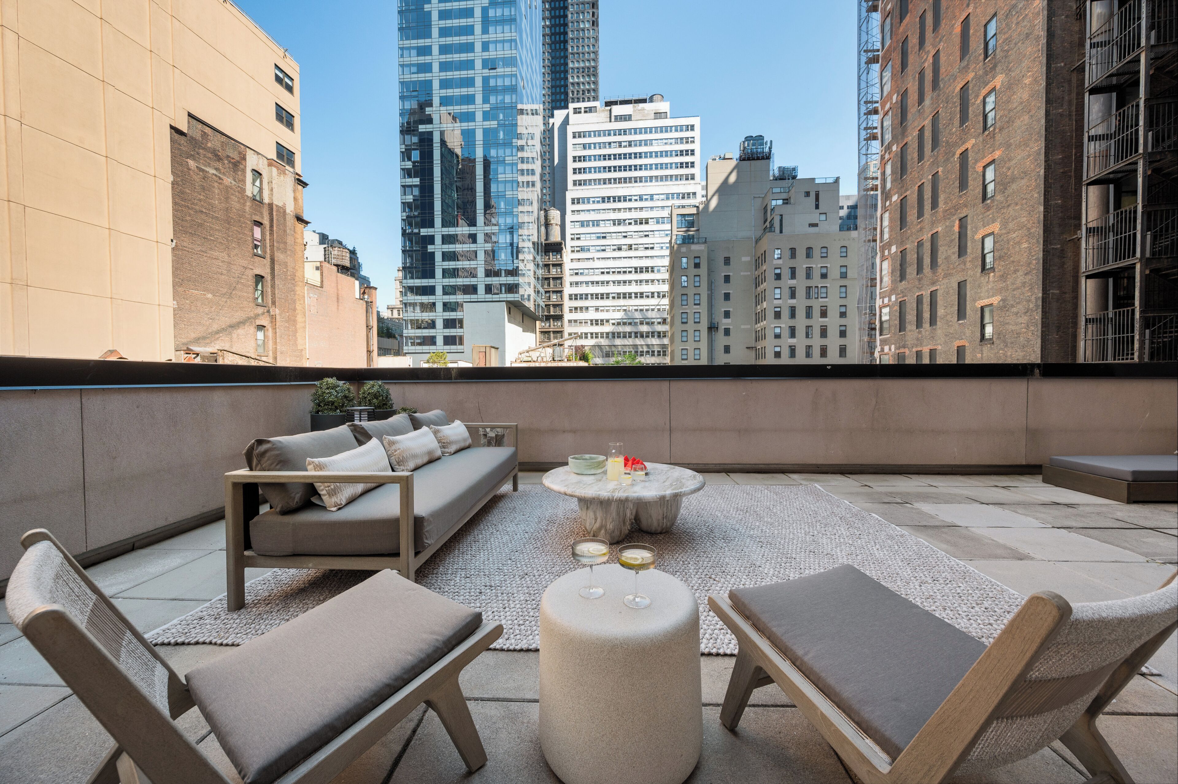 A rooftop terrace with outdoor furniture, a round table, and a view of city buildings.