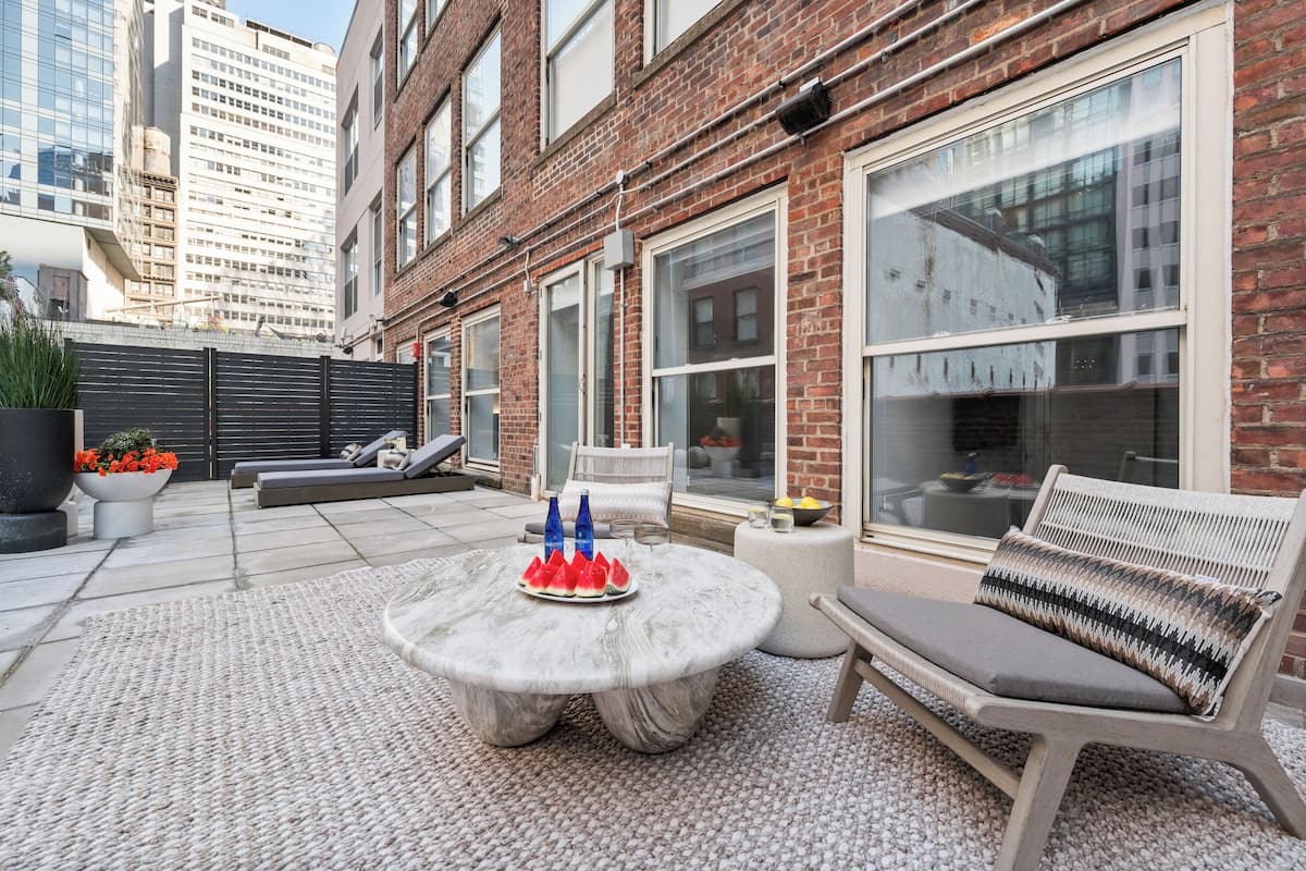 A patio with a round table, outdoor seating, and a brick building in the background.
