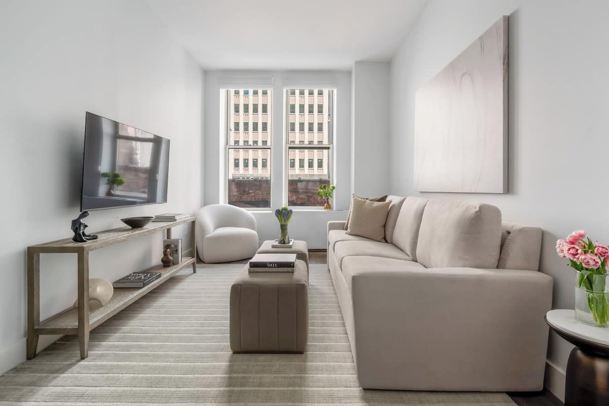 A modern living room with a sofa, a coffee table, a TV, and a window with a city view.