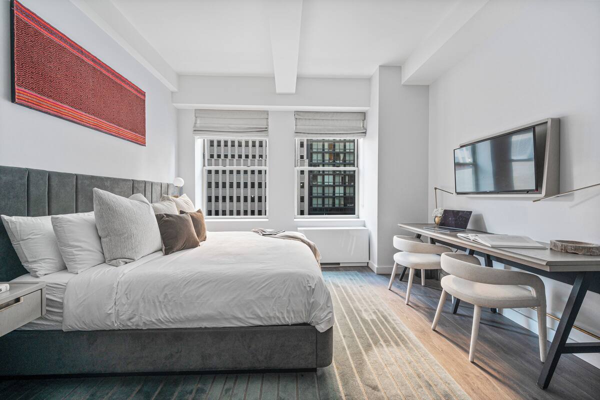 A modern bedroom with a large bed, a desk, and a TV.