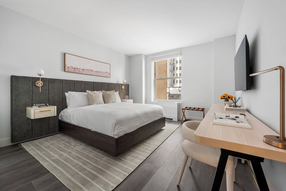A modern bedroom with a bed, bedside table, lamp, and a desk with a chair.