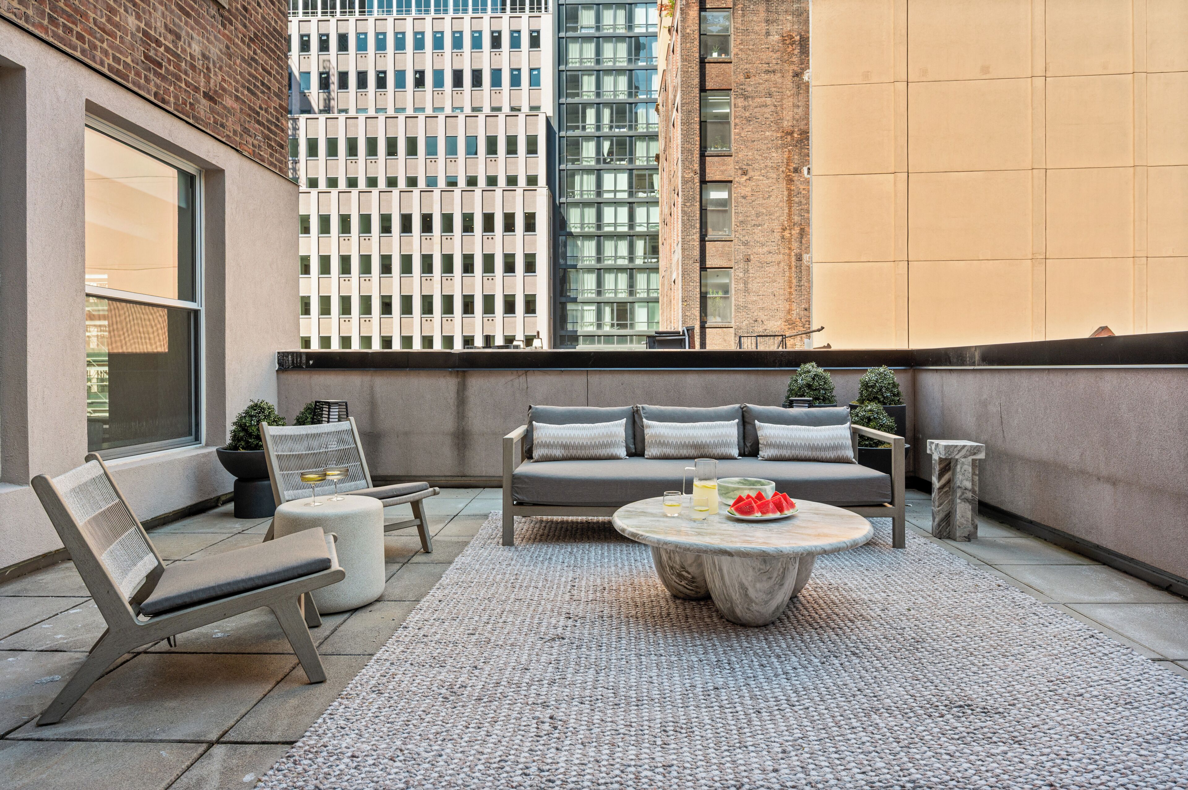 Eine Dachterrasse mit einer Couch, Sesseln, einem Couchtisch und Topfpflanzen.