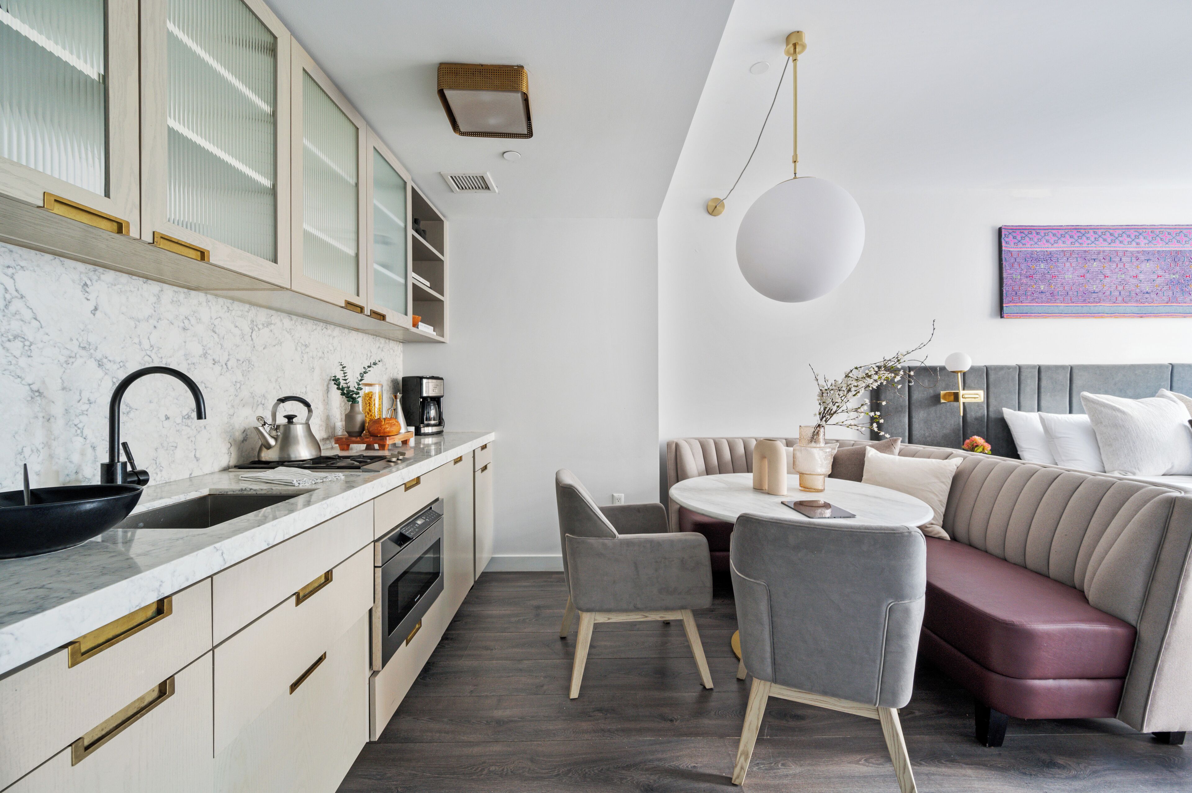 A modern kitchen with a marble countertop, a sink, and a stove. There is a dining area with a round table and chairs.
